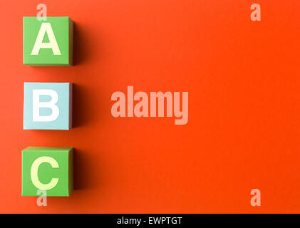 three colorful paper cubes with capital letters, in a row on red background. copy space available Stock Photo