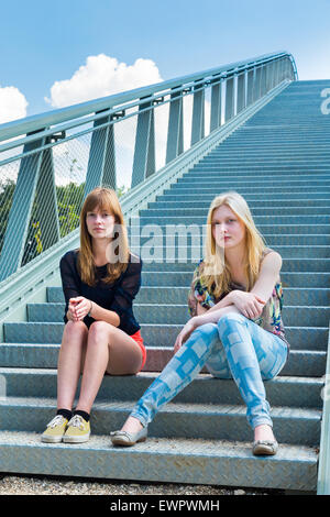 Two caucasian girls sitting on metal bridge Stock Photo