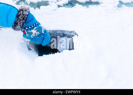 Hand with blue glove scratching ice from windshield of car in winter season Stock Photo