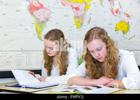 Two caucasian teenage sisters studying in front of wall world chart in classroom on school Stock Photo