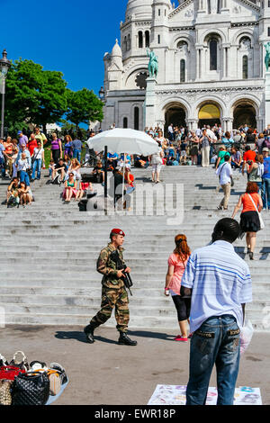 Crowds of tourists, and man selling handbags, Sacre Coeur Basilica, Montmartre, Paris, France, with French soldier walking past Stock Photo