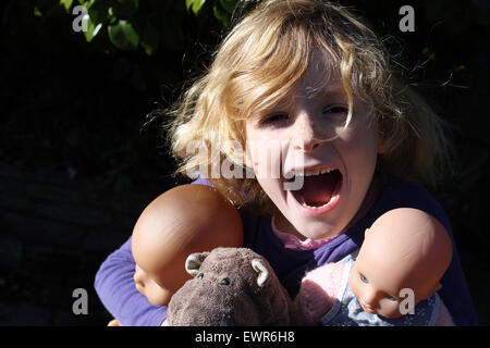 A six year old girl screams with joy as she hugs her most valuable posessions: two dolls and a stuffed hippopotamus Stock Photo