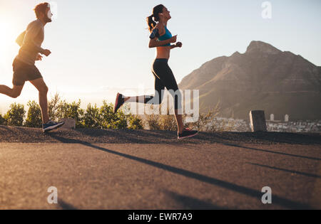 Shot of young man and woman running on country road. Young couple training in nature. Stock Photo