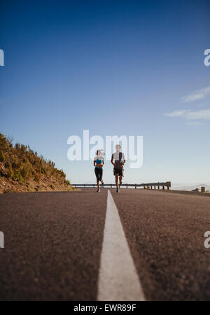 Two young people jogging on country road, low angle distant shot of runners running on open road on  a summer day. Stock Photo