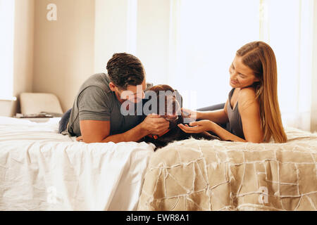 Shot of a young couple with their dog on the bed in morning. Young man and woman spending time with their pet in bedroom. Stock Photo