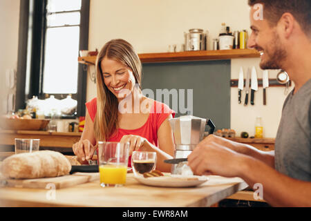 Happy young couple having breakfast together at home. Young woman and man smiling while eating breakfast in kitchen. Couple havi Stock Photo