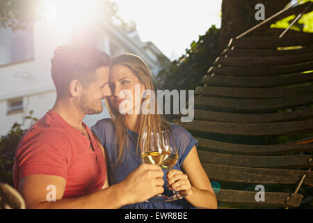 Romantic young couple sitting on garden hammock toasting wine. Loving young couple celebrating with a glass of wine in backyard Stock Photo