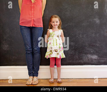 Little girl with sweet smile standing with her mother. Mother is cropped in the picture with focus on little girl looking at cam Stock Photo