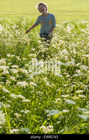 A very happy boy runs through a meadow of cow parsley and long grass in the summertime with the sun shining and very happy Stock Photo