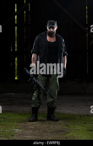 Action Hero Muscled Man Holding Machine Gun - Standing In Abandoned Building Wearing Green Pants Stock Photo