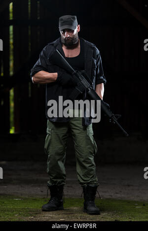 Action Hero Muscled Man Holding Machine Gun - Standing In Abandoned Building Wearing Green Pants Stock Photo