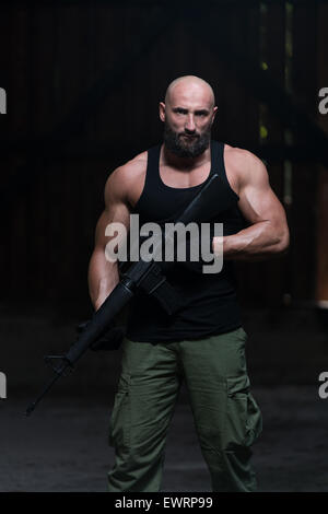 Action Hero Muscled Man Holding Machine Gun - Standing In Abandoned Building Wearing Green Pants Stock Photo