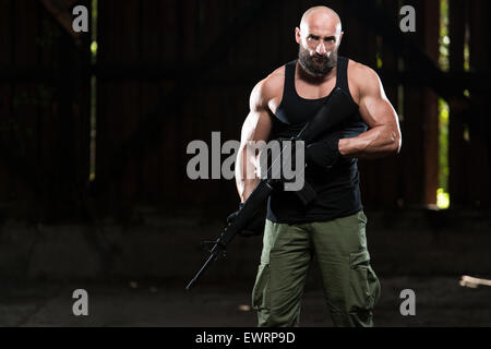 Action Hero Muscled Man Holding Machine Gun - Standing In Abandoned Building Wearing Green Pants Stock Photo