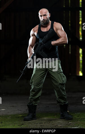 Action Hero Muscled Man Holding Machine Gun - Standing In Abandoned Building Wearing Green Pants Stock Photo