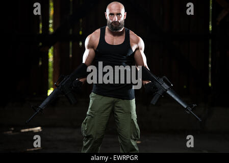 Action Hero Muscled Man Holding Machine Gun - Standing In Abandoned Building Wearing Green Pants Stock Photo
