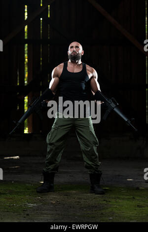 Action Hero Muscled Man Holding Machine Gun - Standing In Abandoned Building Wearing Green Pants Stock Photo