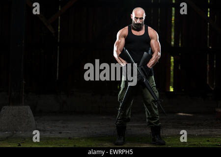 Action Hero Muscled Man Holding Machine Gun - Standing In Abandoned Building Wearing Green Pants Stock Photo