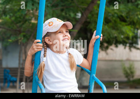 Happy five year old girl riding on a swing at the playground Stock Photo