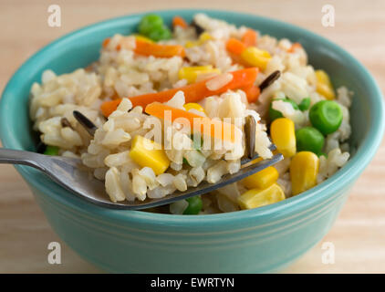 Close view of a bowl of brown and wild rice with peas, carrots and corn with a fork filled in the foreground Stock Photo