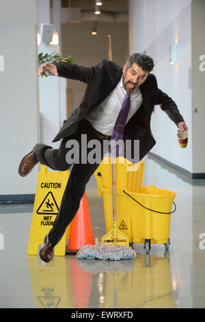 Businessman falling on wet floor inside office building Stock Photo