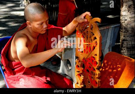 Chiang Mai, Thailand:  Buddhist monk wearing a burgundy-coloured robe painting filigree wooden window tracery at Wat Ku Tao Stock Photo