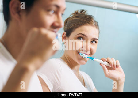Young couple living together, washing teeth in bathroom in the morning. The woman looks happily at her boyfriend. Concept of new Stock Photo