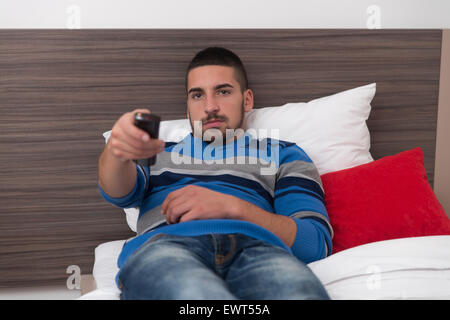 Handsome Young Man Watching Television Lying On Bed With The Remote Control In His Hand Stock Photo