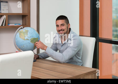 Portrait Of A Man Sitting By His Desk And Holding A Globe Model Stock Photo