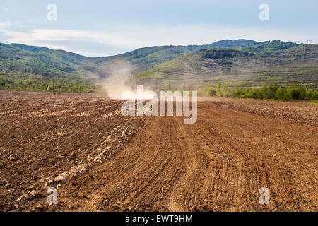 A tractor is cultivating the soil before sowing in the early spring. The machine perform this activity to loosens the soil after Stock Photo