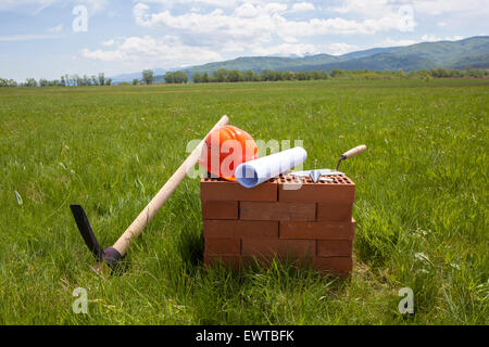 Bricks, trowel, blueprint on a roll, plummet, pick axe and hardhat prepared for beginning of construction of a new building. The Stock Photo