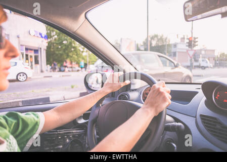 Adult woman driving car with hands on steering wheel. Interior close up, selective focus on one hand, side view. Stock Photo