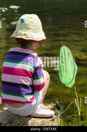 Young girl looking for fish to catch in her green net in summertime Stock Photo