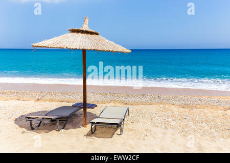 Reed beach umbrella with two loungers on beach near blue sea coast in Greece Stock Photo