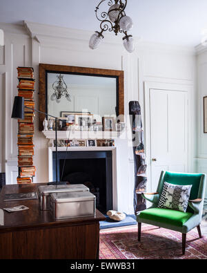 Mid century green armchair in study with persian rug, mantelpiece and stacked books Stock Photo