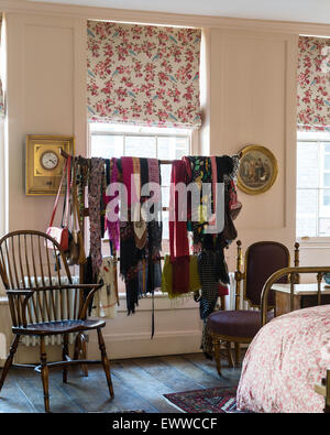 Assorted scarves hung on a chinese clothes rack in bedroom with floral patterned blinds and windsor chair Stock Photo