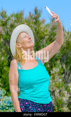 Middle aged woman taking a selfie photo of herself on a hot sunny day in Summer in the UK. Stock Photo