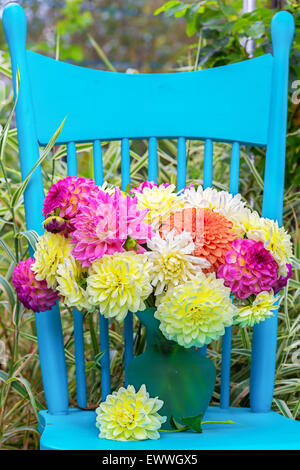 A vase of dahlia cut flowers on a pretty blue chair in the garden. Stock Photo