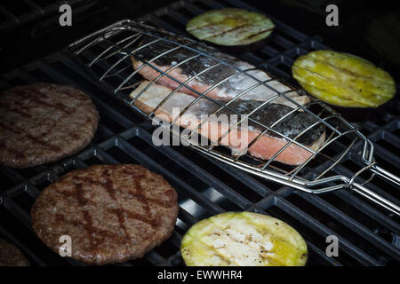Salmon steak, hamburger slices and eggplant on grill rack, soft focus Stock Photo