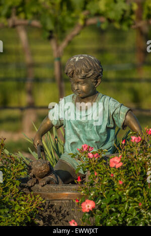 Bronze boy and dog garden statue placed in flower garden near vineyard Stock Photo