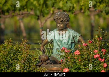 Bronze boy and dog garden statue placed in flower garden near vineyard Stock Photo