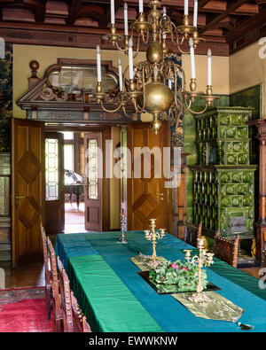 Brass chandelier above long dining table in room with green tiled stove Stock Photo