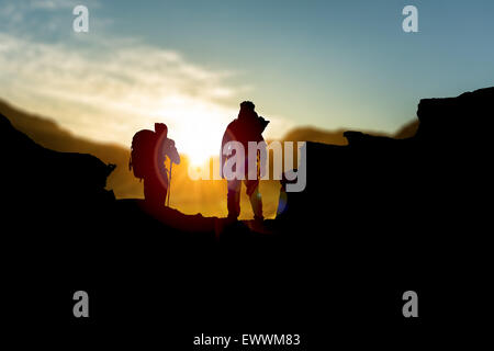 silhouette of people hiking up a mountain, set against a setting sun in the sky Stock Photo