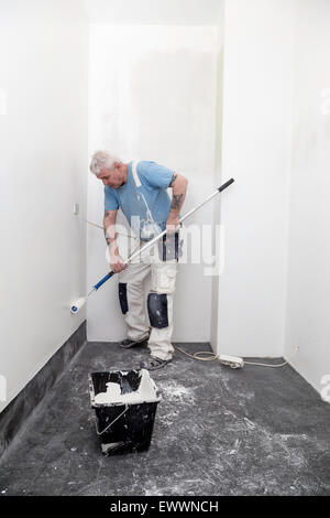 Painter painting walls white in a home, bucket full of paint in front of him Stock Photo