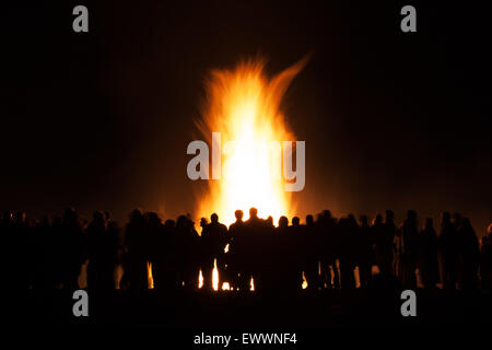 Silhouttes of a group of people watching a bonfire set against the flames and black night Stock Photo