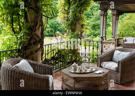Wicker garden furniture on terrace with wisteria-clad columns and iron balustrade Stock Photo
