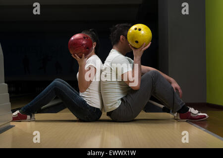 Young Couple Hiding Their Faces Behind Bowling Ball Stock Photo