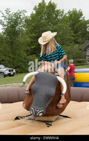 Young pre-teen girl rides a mechanical bull at the Canada Day celebrations in Cannington, Ontario Stock Photo