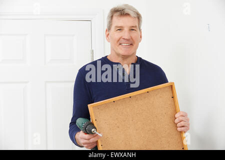 Mature Man Drilling Wall To Hang Picture Frame Stock Photo