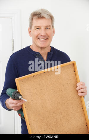 Mature Man Drilling Wall To Hang Picture Frame Stock Photo