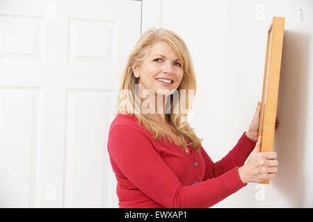 Mature Woman Hanging Picture On Wall Stock Photo